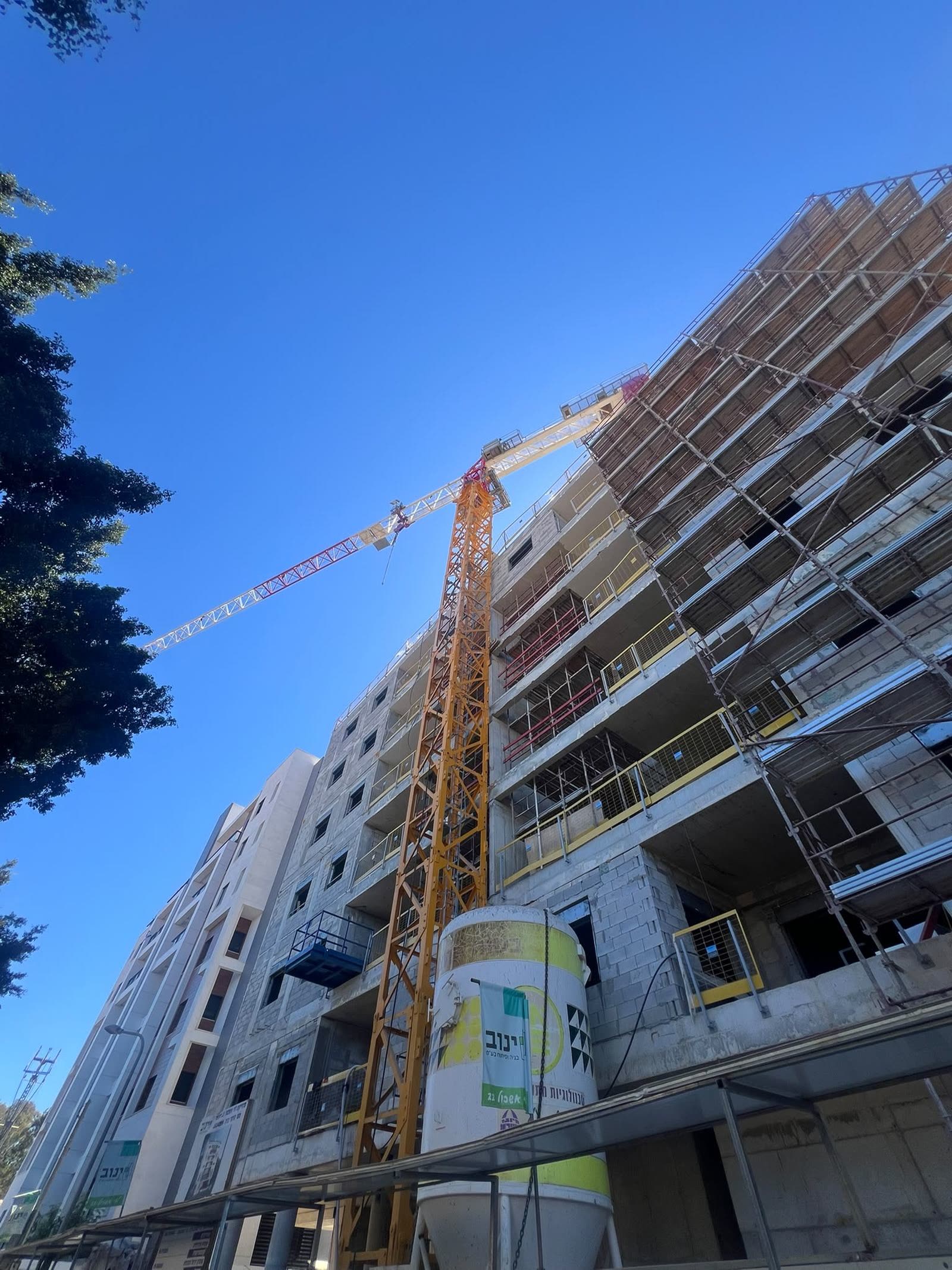 עגורן צריח צהוב של קלמן ברדה באתר מגורים ברעננה, צילום מלמטה על רקע שמיים כחולים