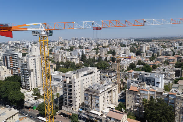 מבט אווירי על זרוע עגורן צריח חשופה מעל גגות שכונת מגורים ברחובות