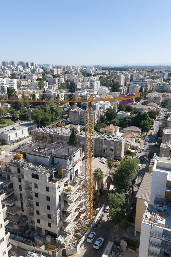 עגורן צריח צהוב של קלמן ברדה עומד לצד בניין מגורים בהקמה, קו רקיע רחובות ברקע