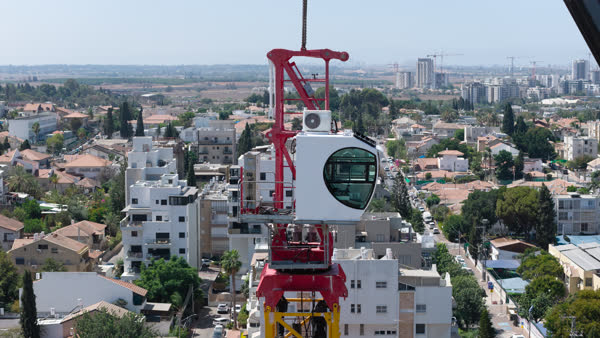 תקריב על תא ההפעלה האדום-לבן של עגורן הצריח מעל קווי הרקיע של רחובות