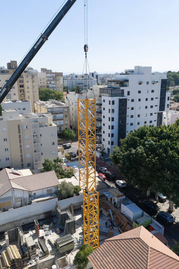 מנוף נייד מרים קטע תורן של עגורן צריח בין בנייני מגורים ברחובות